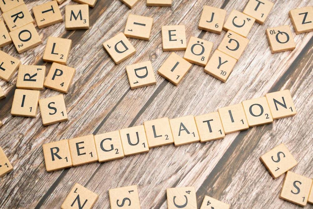 A collection of wooden letter tiles scattered on a wooden surface, with the word 'REGULATION' prominently displayed in the center.